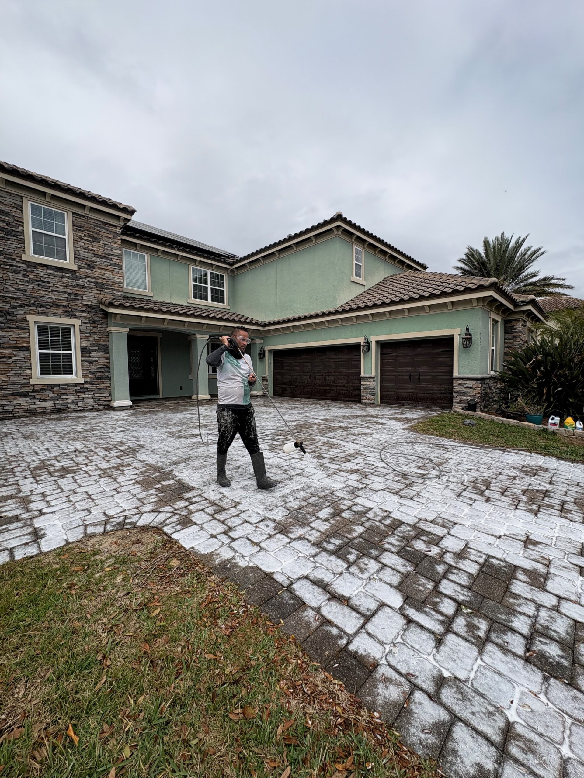 Third Coat technician pressure washing a paver driveway in front of luxury Orlando home