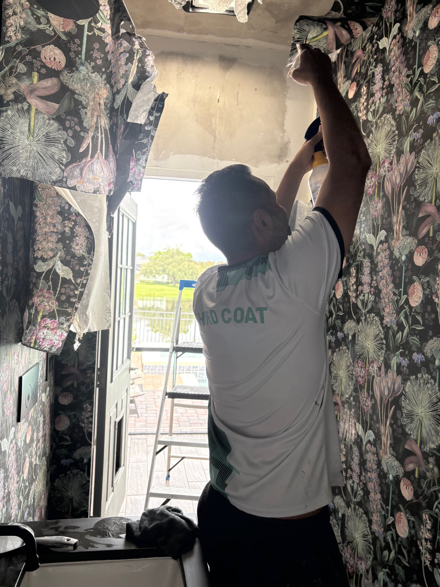 Third Coat painter removing dark floral wallpaper from luxury powder room, professional wallpaper removal in Orlando